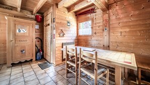 Een houten blokhutinterieur met een eettafel, stoelen, een kast, een raam en een rode em met de tekst 'INCENDI'.