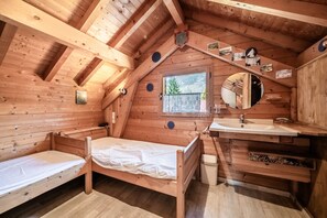 A wooden cabin with a loft bedroom, a window, a mirror, and a sink. - Chalet “6p Classique - Clématite” with Mountain View, Private Terrace & Wi-Fi (Verchaix)