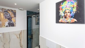 Un interior moderno con paredes de mármol, una cabina de ducha de vidrio y dos cuadros coloridos.