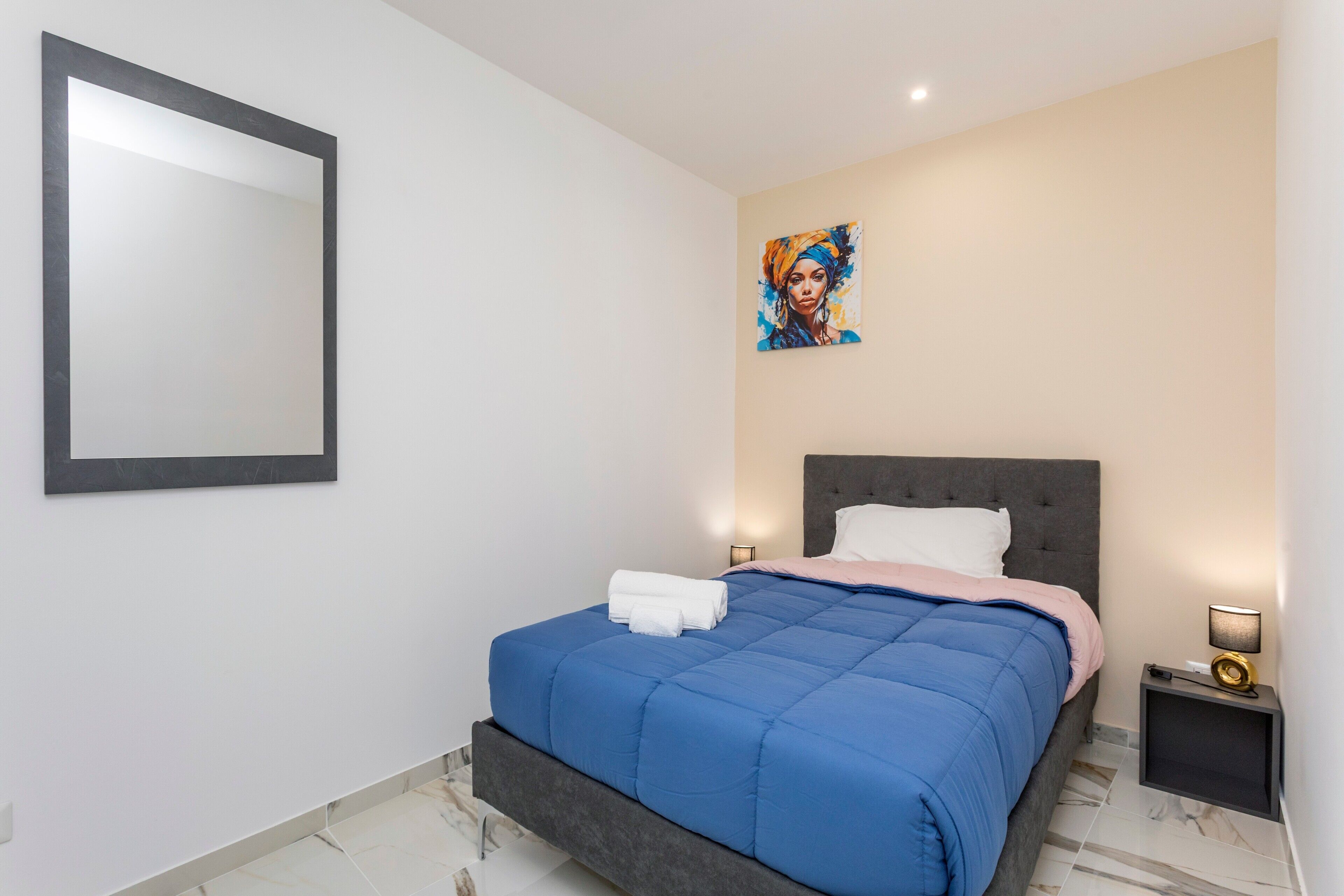 Une chambre à coucher avec un lit, une table de chevet, un miroir fixé au mur et un tableau.