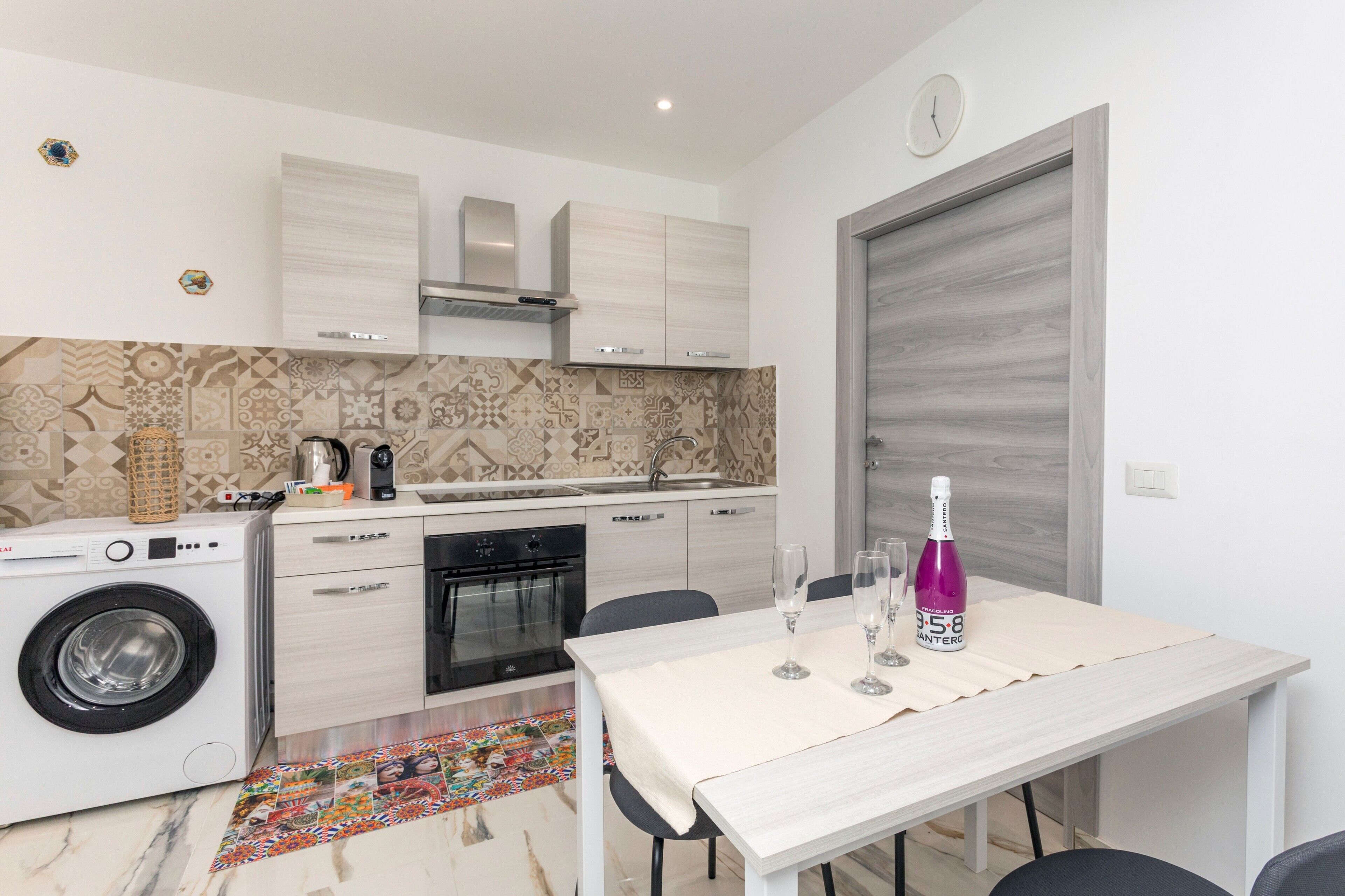 Een kleine keuken met een wasmachine, een eettafel met stoelen en een decoratieve spatwand.
