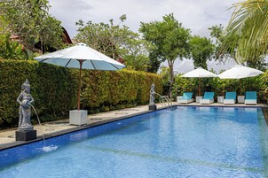 A swimming pool with lounge chairs and umbrellas, surrounded by greenery and statues.