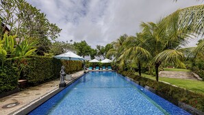Une piscine entourée de plantes tropicales et agrémentée d’une statue, avec des chaises longues et des parasols à proximité.