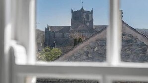 A view of a stone building with a clock tower, through a window with a white frame. - Gatehouse Cottage, Cartmel (Cartmel)