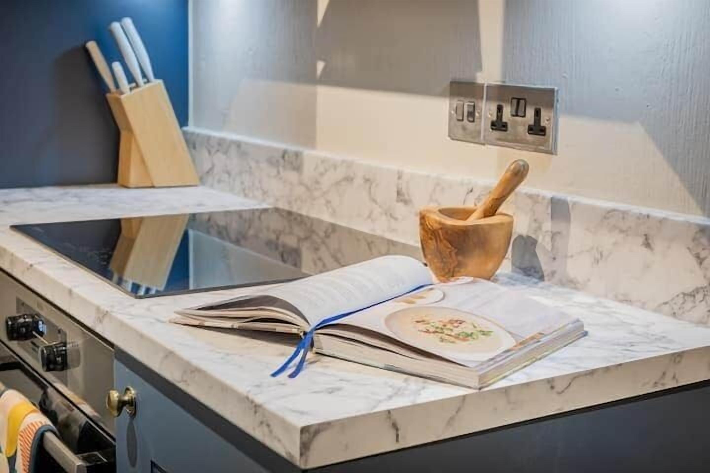 A kitchen counter with a marble surface, a book, a wooden rolling pin, and a knife holder.