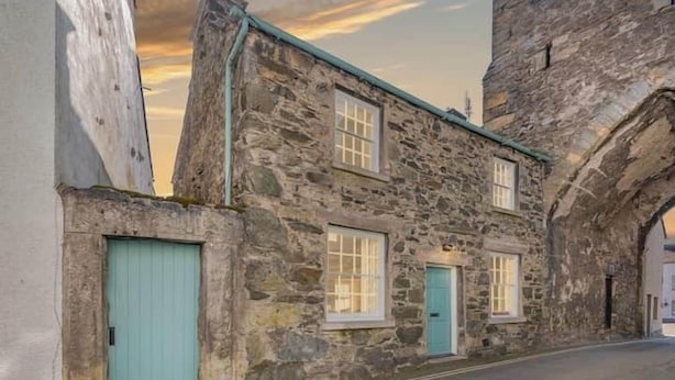 A stone building with a teal door and windows, a narrow street, and an archway. - Gatehouse Cottage, Cartmel (Cartmel)