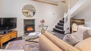 A living room with a TV, fireplace, sofa, and staircase. - Gatehouse Cottage, Cartmel (Cartmel)