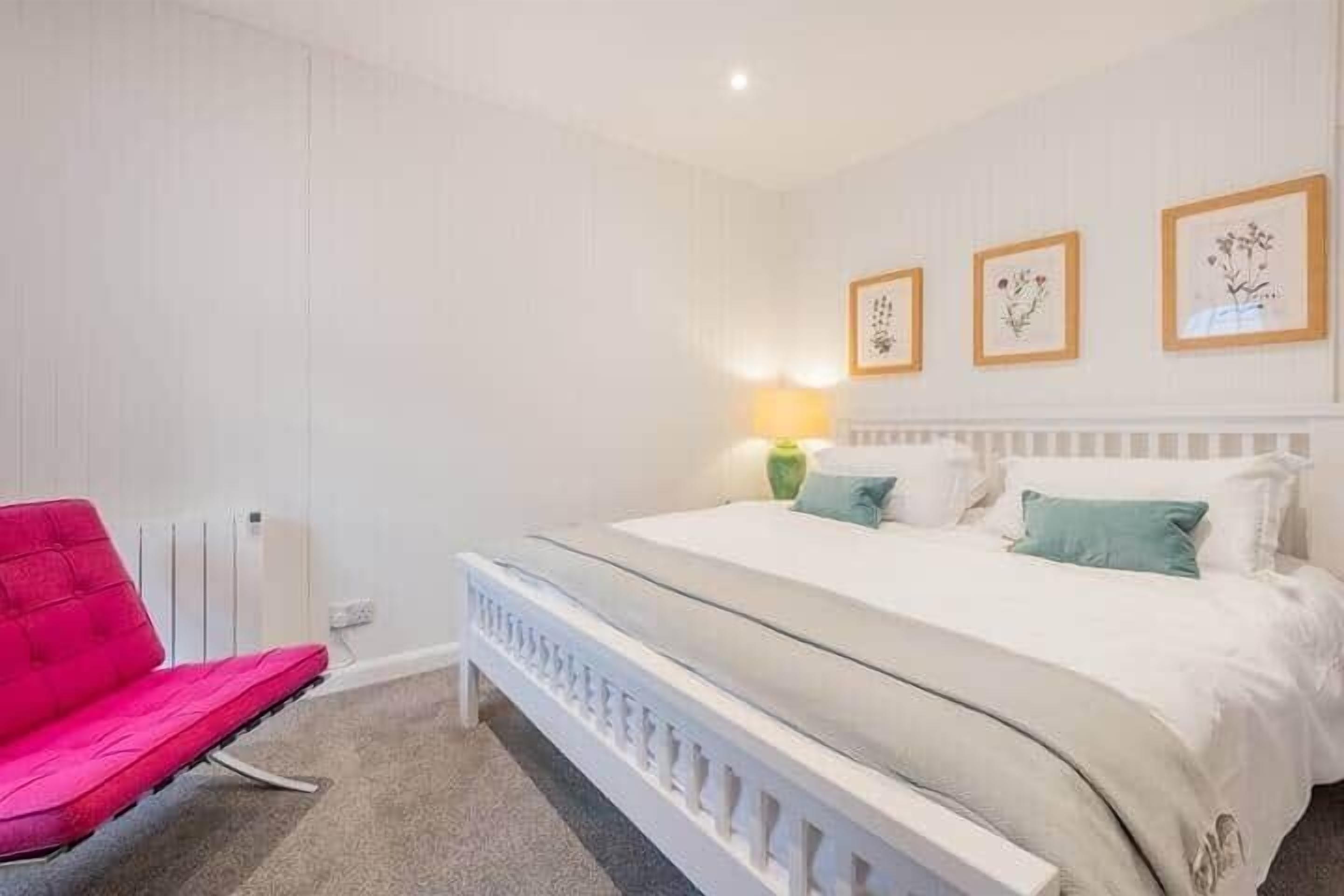 A bedroom with a bed, a chair, and framed botanical prints on the wall.