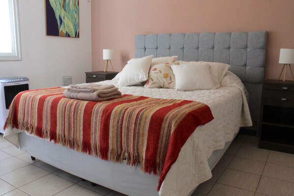Un lit bien fait, recouvert d’une couverture à rayures, deux tables de chevet avec des lampes et un tableau accroché au mur.