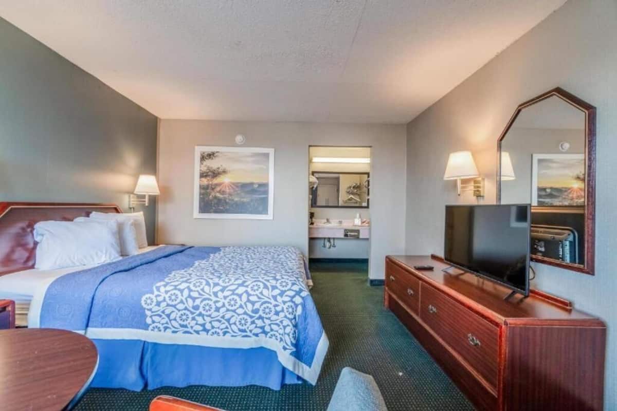A hotel room with a bed, a desk, a dresser, a TV, and a bathroom visible through an open door.
