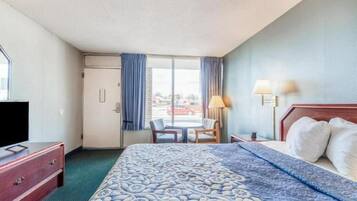 Una habitación de hotel con cama, escritorio, silla, televisor y ventana con cortinas.