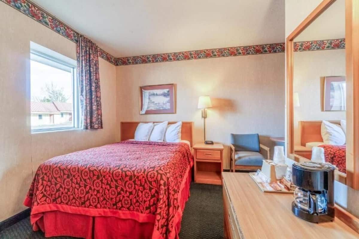 A hotel room with a bed, a chair, a desk with a coffee maker, a lamp, and a window with curtains.