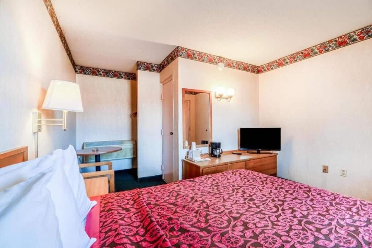 A hotel room with a bed, a desk, a chair, a television, and a lamp.