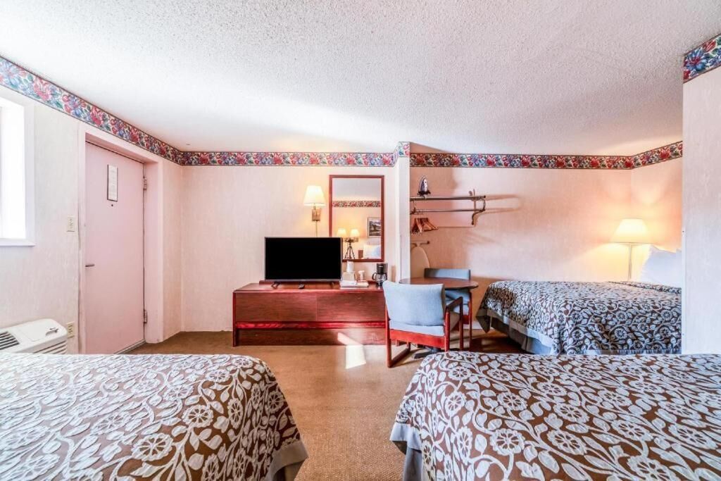 A hotel room with two beds, a TV, a desk with a chair, and a small table.