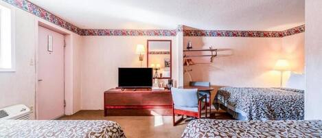 A hotel room with two beds, a TV, a desk with a chair, and a small table.