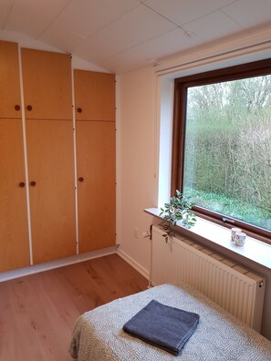Ein Schlafzimmer mit einem Bett, einem Fenster mit Blick auf Bäume, einem Heizkörper und einem Kleiderschrank.