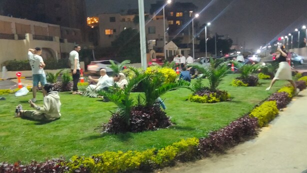 A nighttime outdoor area with people sitting and walking, surrounded by greenery and a paved walkway. - Star House: Steps to Grand Egyptian Museum (Giza Governorate)