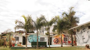 A row of colorful, artistically decorated cabins with murals, surrounded by palm trees and a clear sky. - Pousada Recanto Bella Rosa (Imbituba)