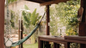 A hammock tied between wooden posts, a white pot with flowers, and a wooden table with a book and a teapot. - Pousada Recanto Bella Rosa (Imbituba)