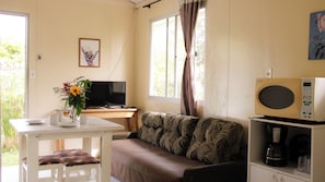 A room with a sofa, a table with a vase of flowers, a television, and a microwave. - Pousada Recanto Bella Rosa (Imbituba)