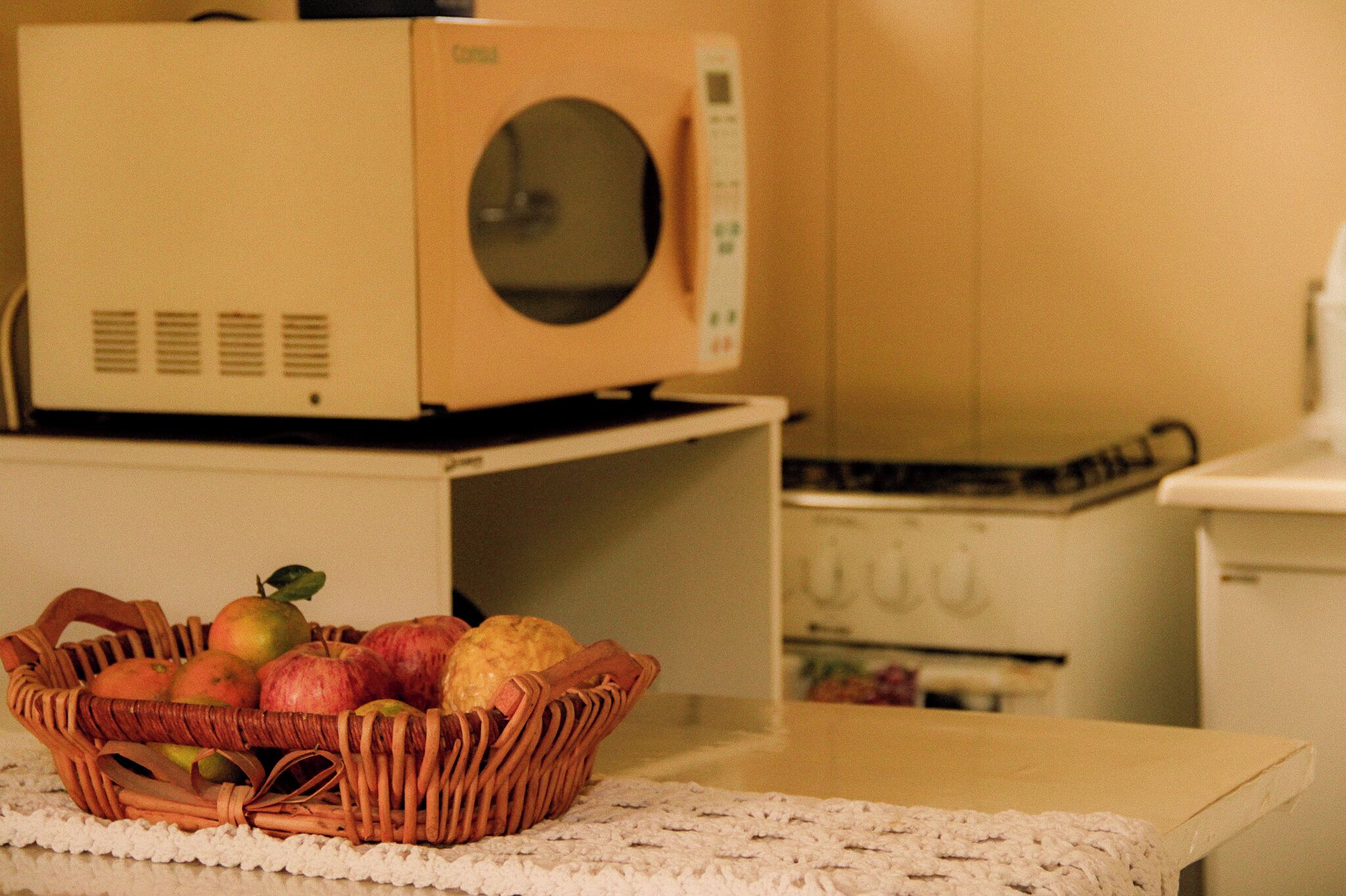 A kitchen with a microwave on a counter, a basket of fruit, and a stove.