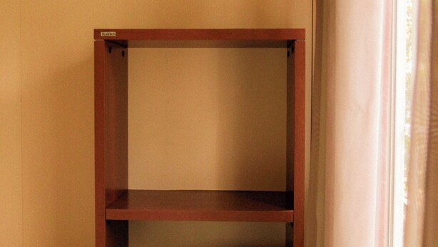 Een stapelbed met houten frame en matras in een kamer met beige wanden.