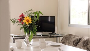A dining table with a vase of flowers, a television, and a sofa in a room with a window. - Pousada Recanto Bella Rosa (Imbituba)