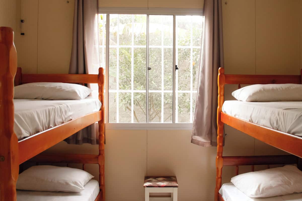 A room with two wooden bunk beds, a small white table, and a window with curtains.