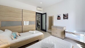 Een moderne slaapkamer met twee bedden, een houten garderobe, een dressoir en een klein bureau.