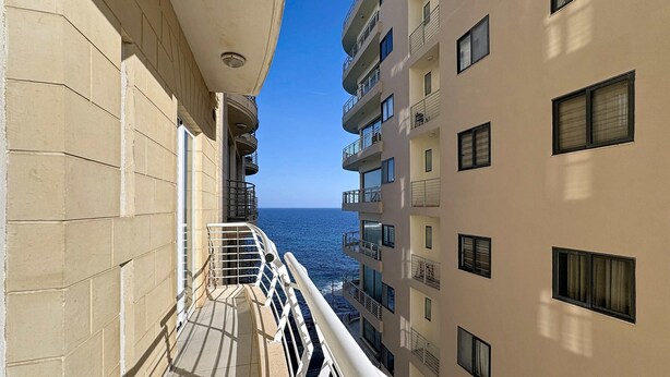 Een balkon met uitzicht op de zee, omliggende gebouwen en een heldere lucht.