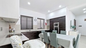 Een moderne keuken met donkere kastjes, een magnetron en een spoelbak. Er staat een eettafel met stoelen en een kinderstoel.