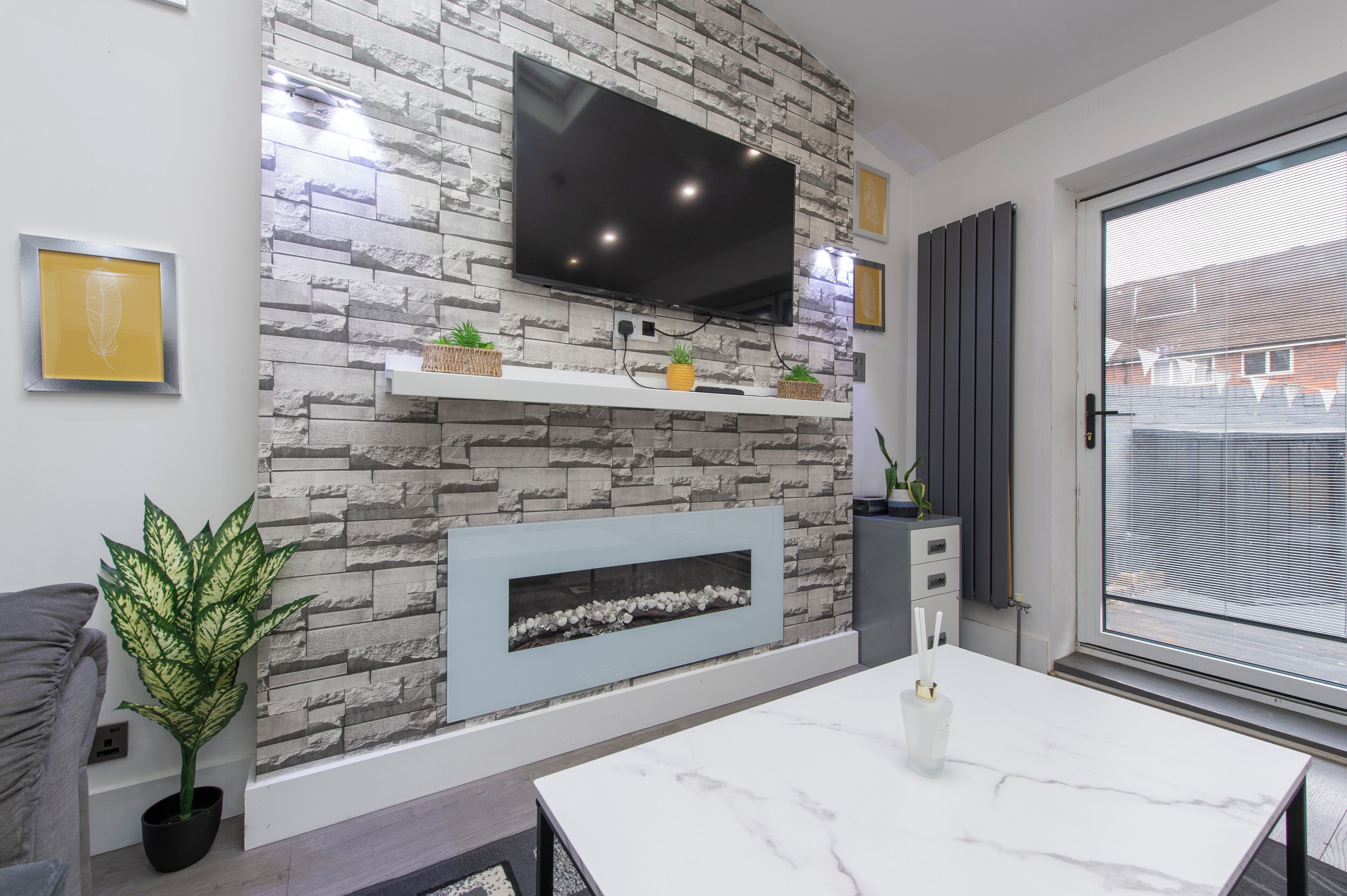 A modern living room with a stone wall, a flat-screen TV, a fireplace, and a dining area.