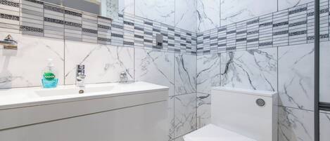 A bathroom with a white marble sink, a toilet, and a patterned tile backsplash.