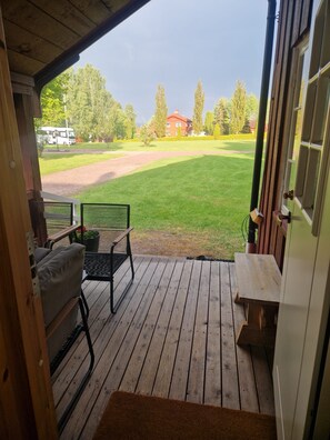 A wooden deck with a bench and a table, overlooking a green lawn and a red building.