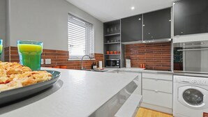 Une cuisine moderne dotée d’un plan de travail blanc, d’un four encastré, d’un four à micro-ondes et d’un lave-linge.