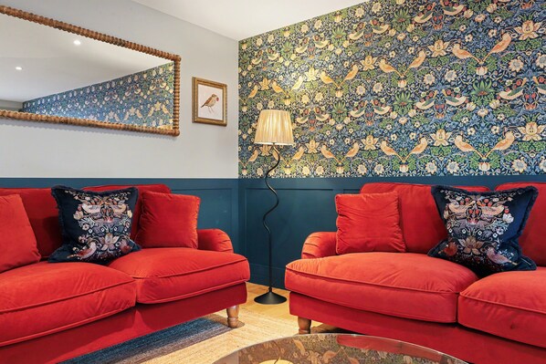Una habitación con dos sofás rojos, un espejo, un papel tapiz con estampado floral y una lámpara de pie.