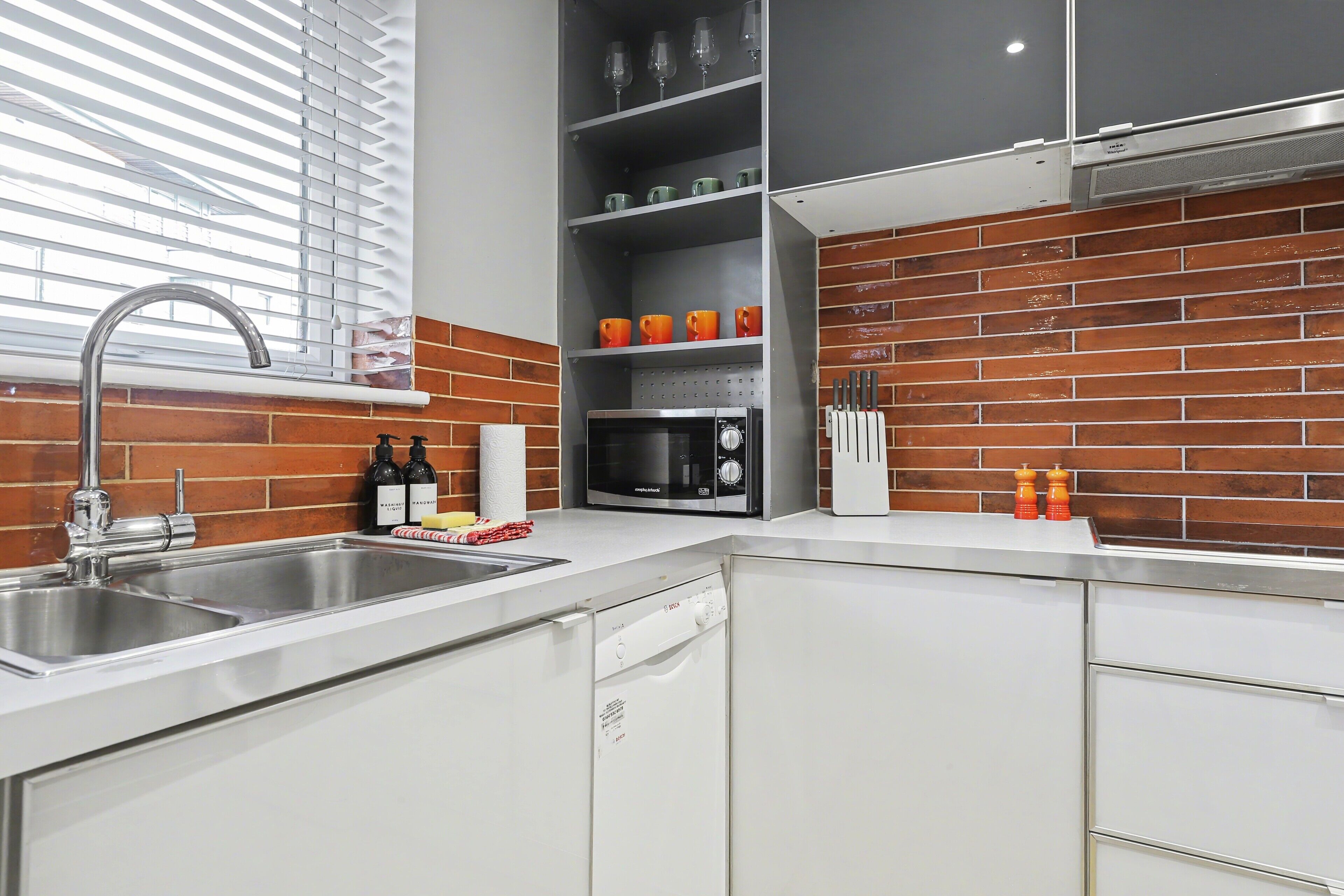 A modern kitchen with a stainless steel sink, a microwave, and a dish rack.