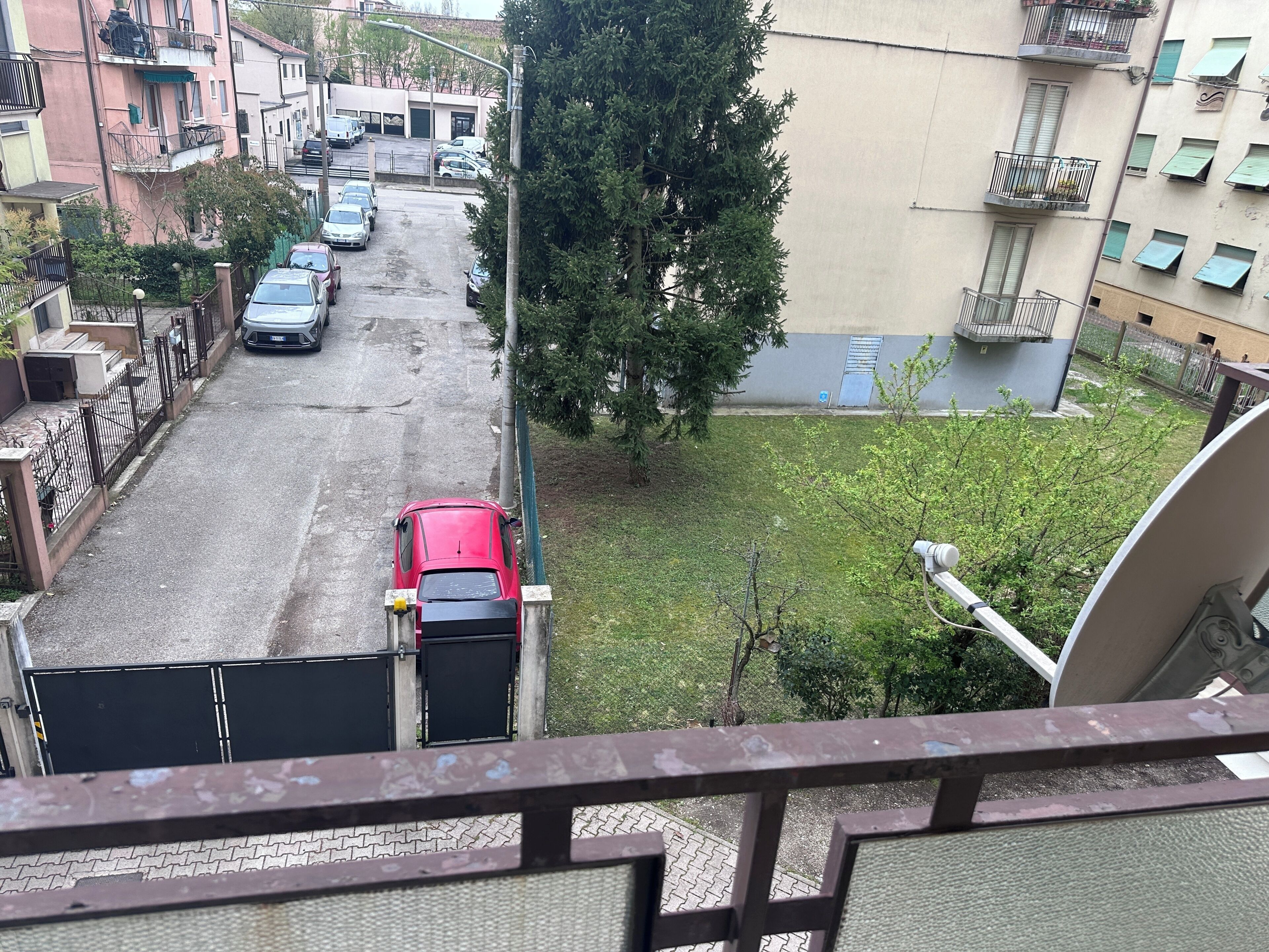 A residential street with parked cars, a red vehicle, and a building with balconies.