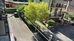 Eine Wohnstraße mit Baumallee, einem parkenden Auto und einem Gebäude mit Balkon.