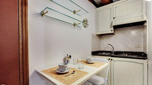 A compact kitchen with white cabinets, a black countertop, and a small dining area with a table and chairs. - Leo Apartment (Venezia)