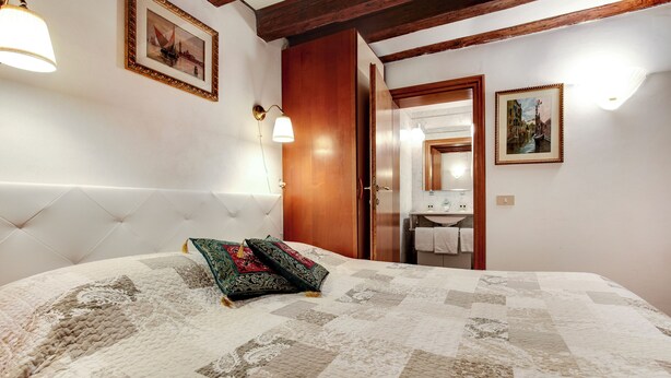 A bedroom with a large bed, a wooden wardrobe, and a bathroom visible through an open door. - Leo Apartment (Venezia)