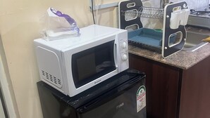 Una cocina compacta con un microondas sobre un refrigerador, un lavamanos con un escurreplatos y una cesta morada.