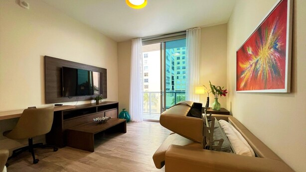 A hotel room with a TV, a sofa, a desk, and a balcony with a view of buildings. - Rent Apart Hollywood (Hollywood)