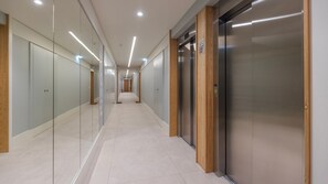 A modern hallway with glass partitions, a wooden floor, and a central elevator. - Gorgeous Apartment with city view by LovelyStay (Algés)