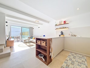A modern kitchen with a central island, a dining area with a glass door leading outside, and a small seating area with a sofa and coffee table. - Villa with private pool and large patio (Los Alcazares)