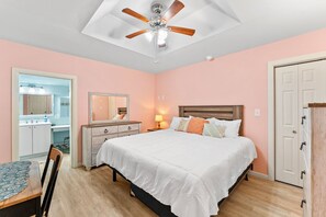 Ein Schlafzimmer mit Bett, Nachttisch, Kommode, Deckenventilator und einer Tür.