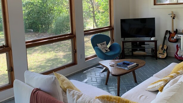 Un salon spacieux doté de grandes fenêtres, d’un ventilateur de plafond, d’une télévision et d’une guitare.