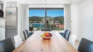 A modern dining area with a wooden table, a bowl of fruit, and a view of a coastal landscape. - Villa High Life - Four Bedroom Villa, Sleeps 9 (Seget Vranjica)
