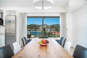 Ein moderner Essbereich mit einem Holztisch, einer Obstschale und Blick auf eine Küstenlandschaft.