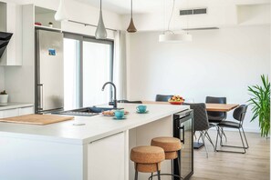 Eine moderne Küche mit einer zentralen Kochinsel, Edelstahlgeräten und einem Essbereich mit Holztisch und schwarzen Stühlen.